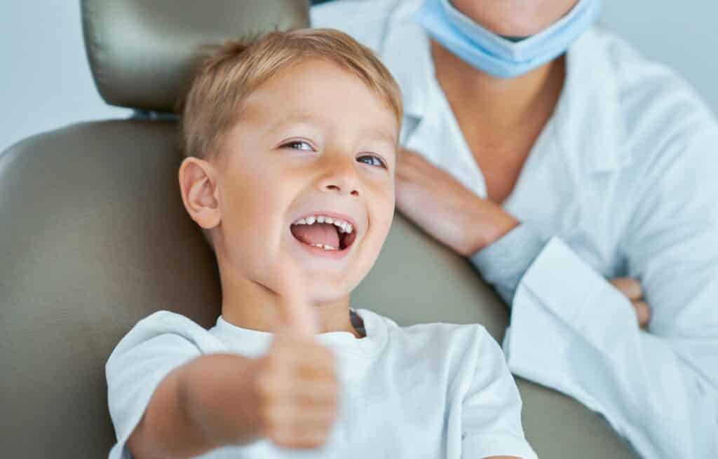 A young boy smiles and gives a thumbs up to the camera