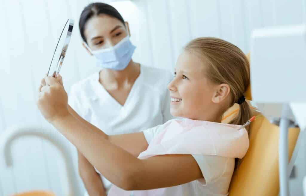 A young girl smiles at herself in a mirror at the dentist